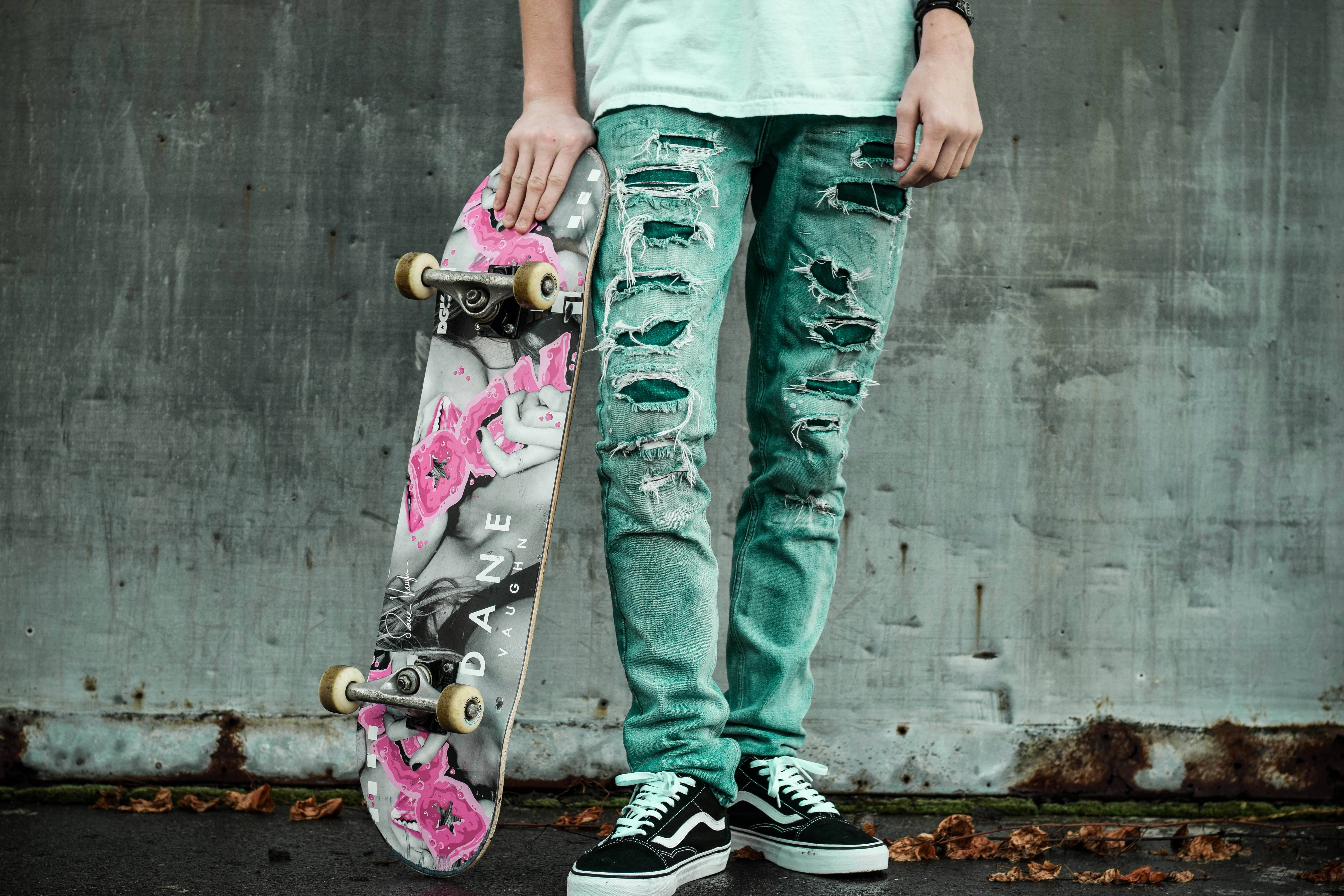 man standing next to wall holding gray and pink skateboard